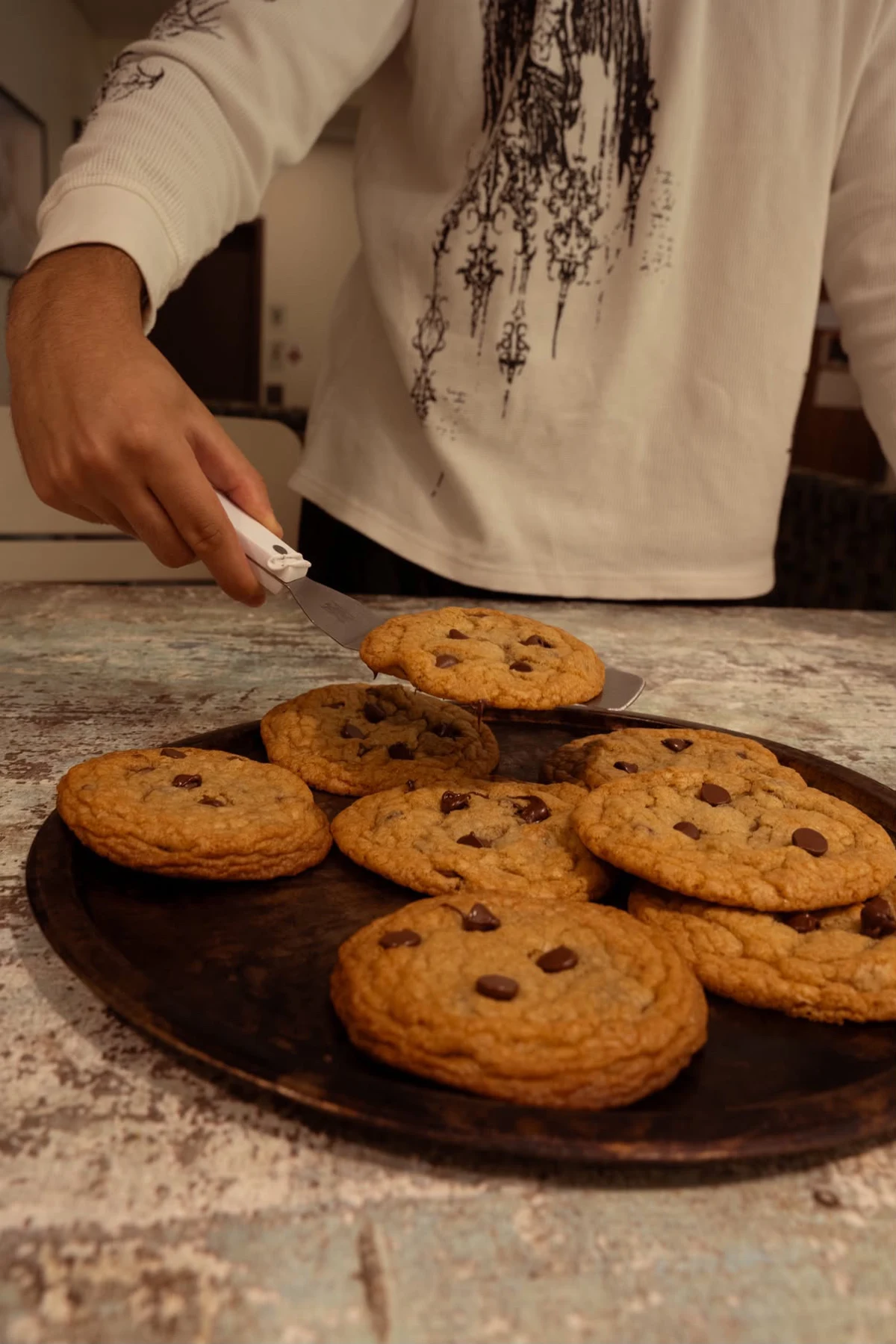 Freshly baked chocolate chip cookies being lifted from a tray
