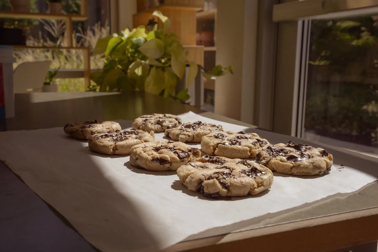 Chocolate chip cookies cooling on parchment beside a sunlit window